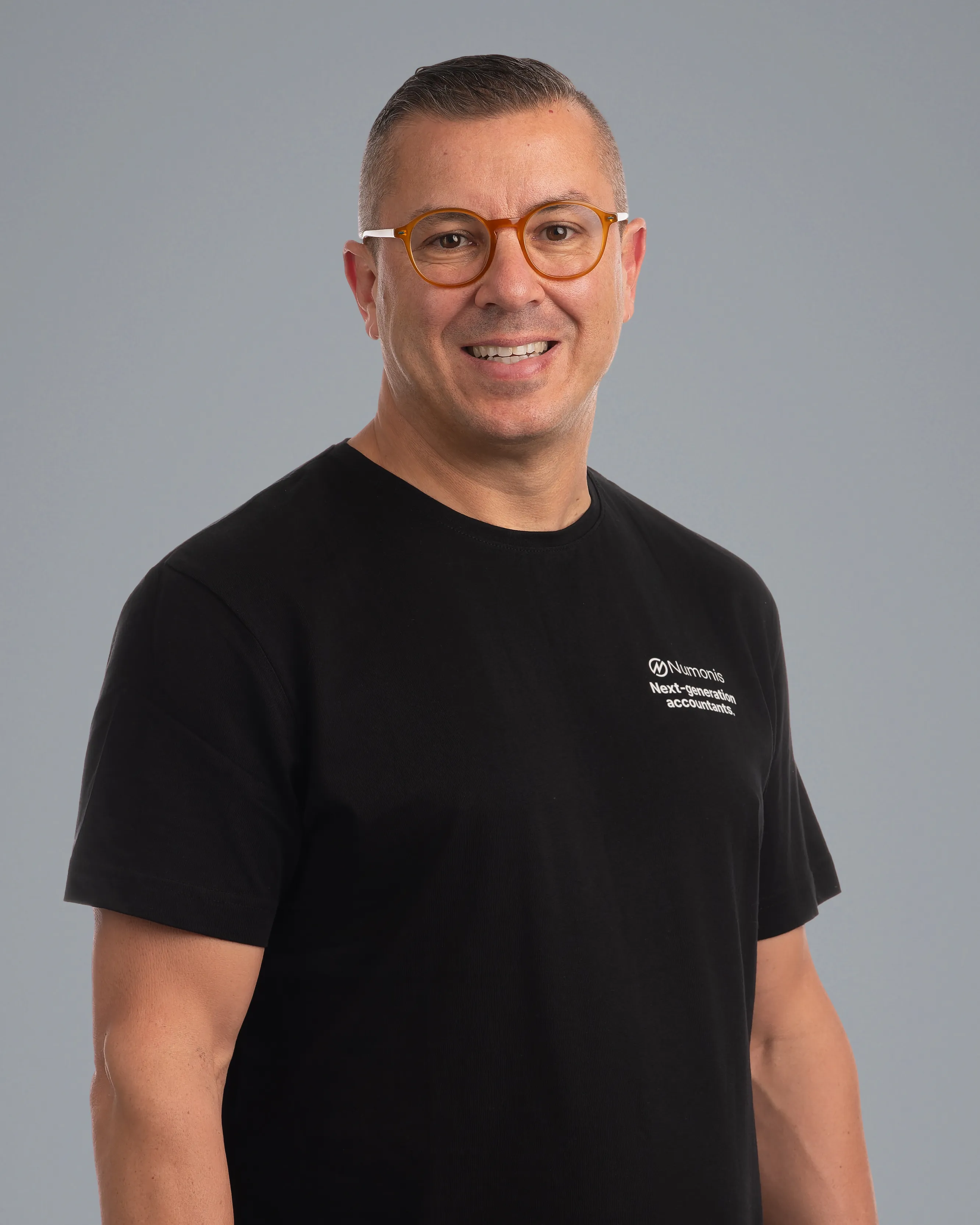 Retrato de Miguel Dominguez, cofundador de Numonis, con gafas y camiseta negra de Numonis sobre fondo gris